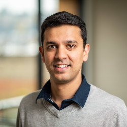 Smiling person with short black hair and a polo shirt under a sweater