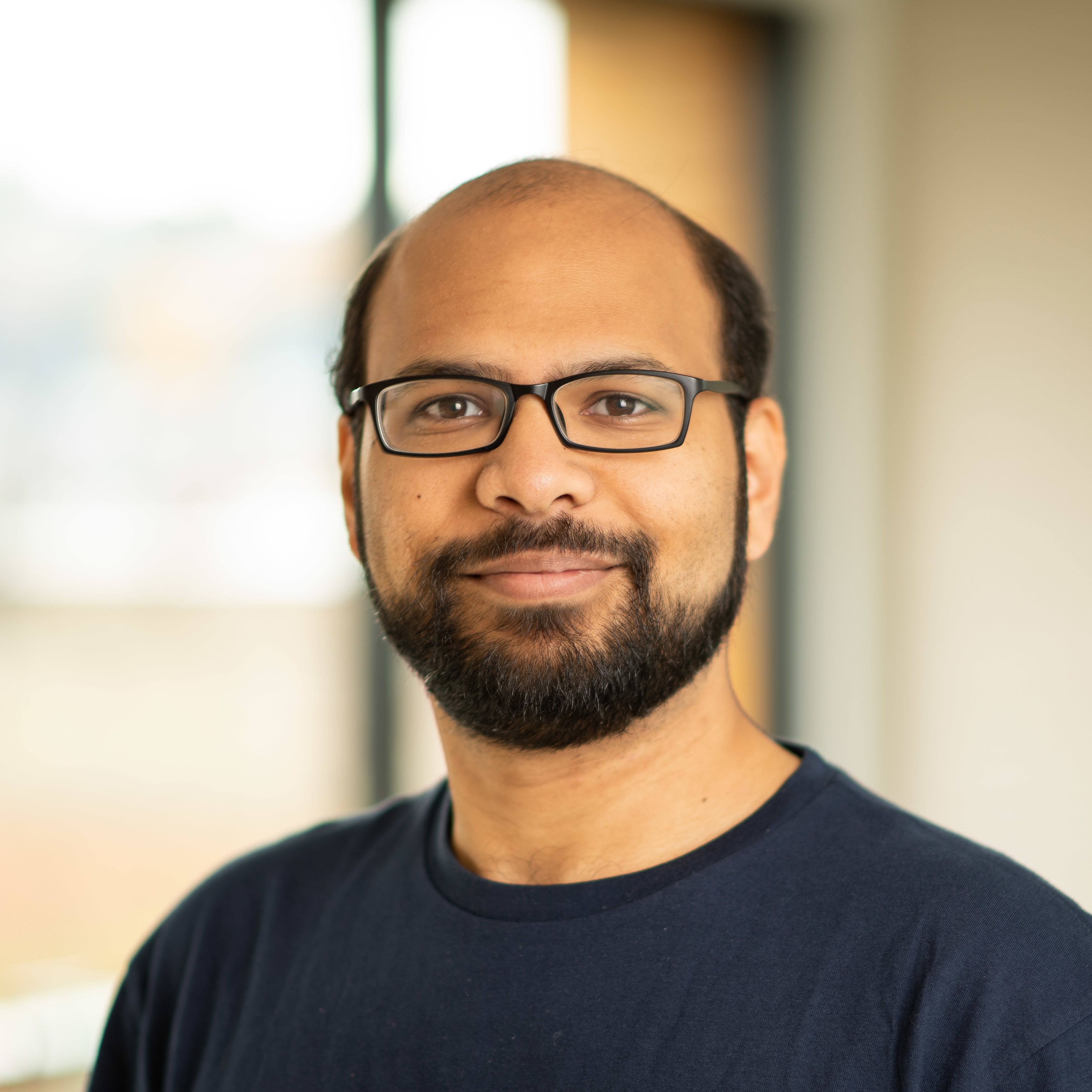 Smiling person with glasses and a beard wearing a dark shirt