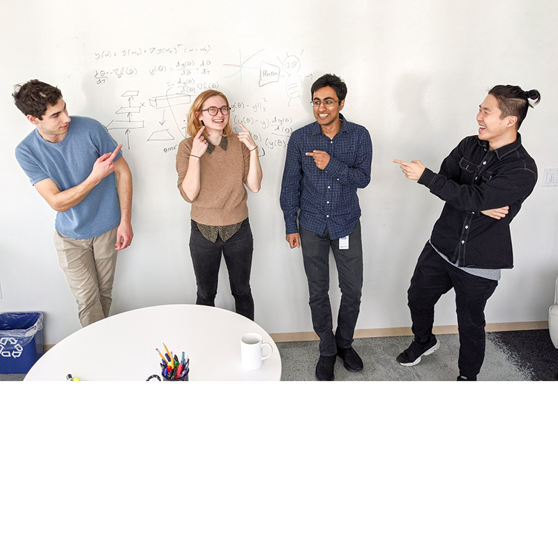 Four young people leaning against a whiteboard talking casually