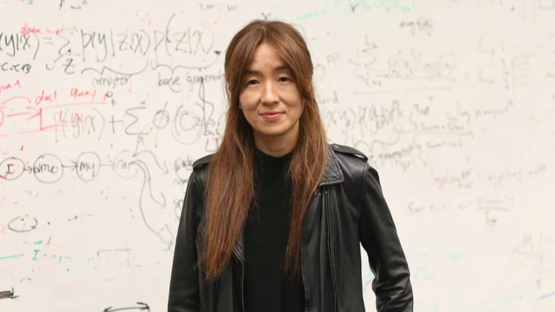 A profile picture of Yejin Choi, a woman with long brown hair wearing a leather jacket and black shirt standing in front of a whiteboard with equations on it.