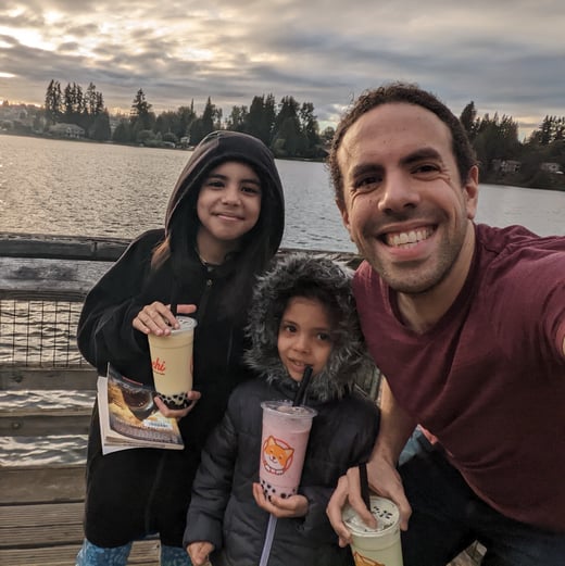 A photograph of Iz Beltagy and his children enjoying Boba tea by the water in Washington.