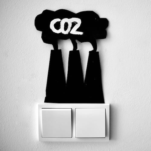 A light switch with a paper cut-out of a series of smokestacks taped above it, with the word 